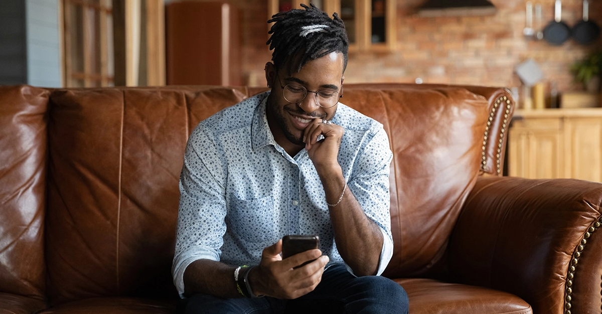 Smiling young african ethnicity guy using smartphone.